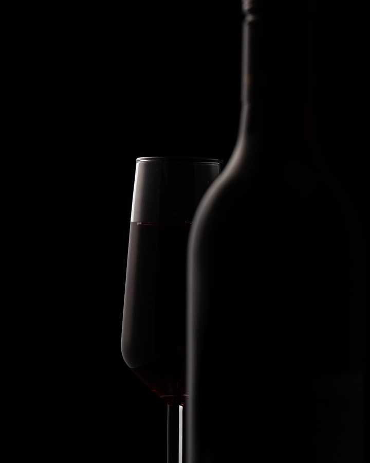 faded black bottle and wine glass on dark background